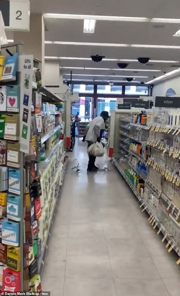 The thief looks back at the security guard on the ground before kicking the shelf beside him, sending more toiletries tumbling to the ground in his wake