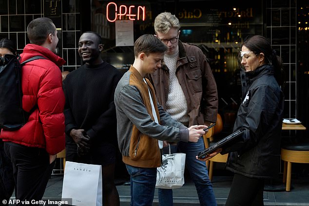 A customer uses their phone to scan a QR code for the NHS Test and Trace in Soho, London. England has now rolled back the need for Covid 'passports' under the recently announced relation of Covid rules