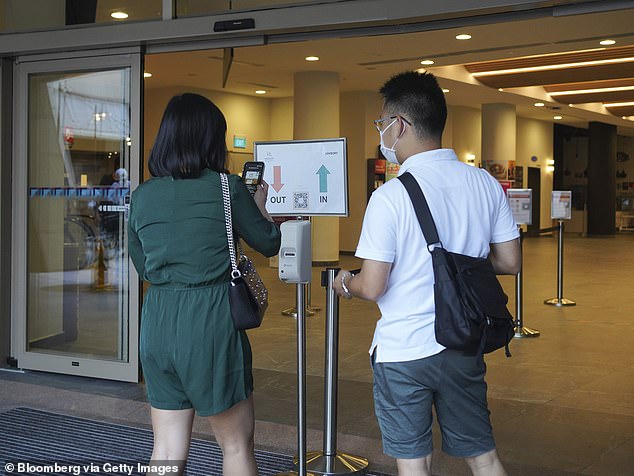 A shopper scans a QR code with a phone at a mall in Singapore. A density limit of one person per 10 square metres applies in shopping malls and large retail stores